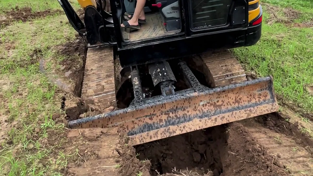 Excavator dozer blade positioned near a ditch during a recovery demonstration