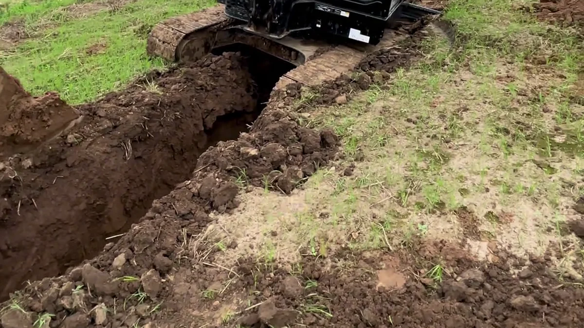 Uneven excavator undercarriage support beside a muddy ditch